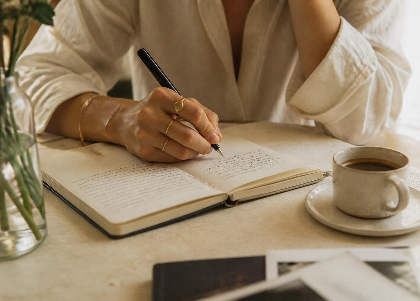 Manos escribiendo en una libreta junto a una taza de café